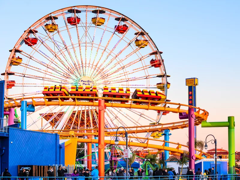 Ferris wheel and roller coaster rides at pier pacific park at sunset with people riding attractions