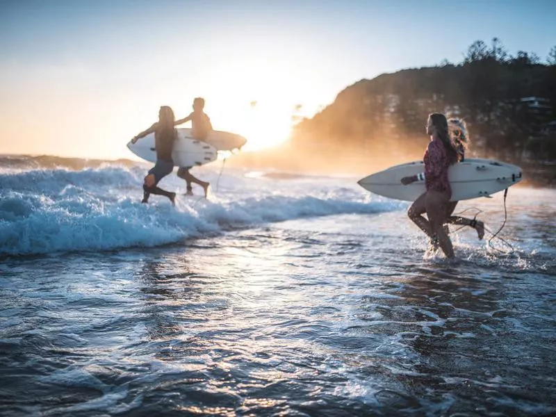 Friends running into the ocean with their surfboards in Australia