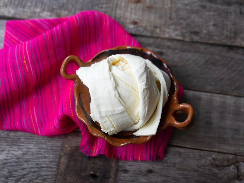 Fresh Oaxaca cheese in clay pot on wood background