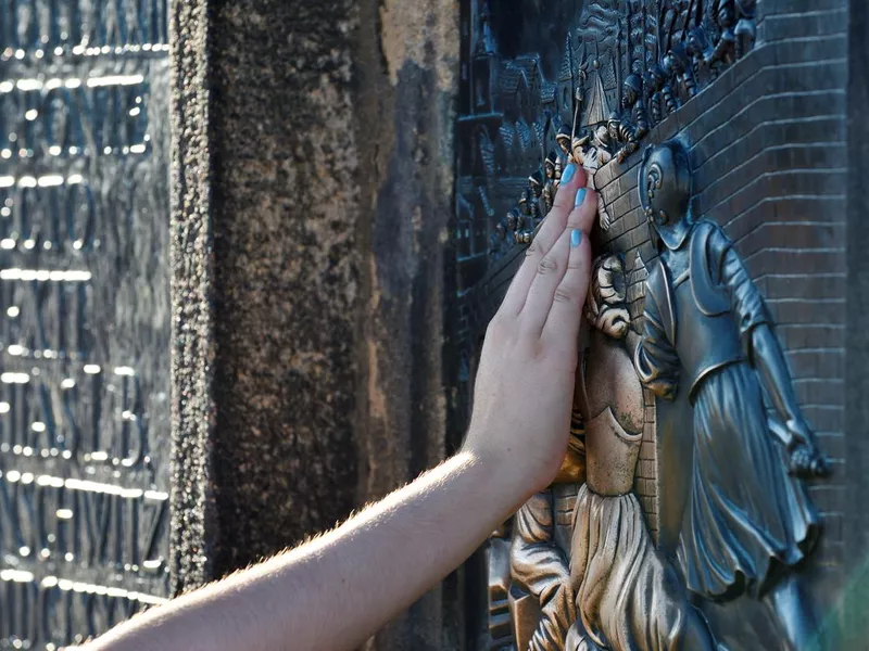 Tourist hand touches Jan Nepomuk on the Charles Bridge