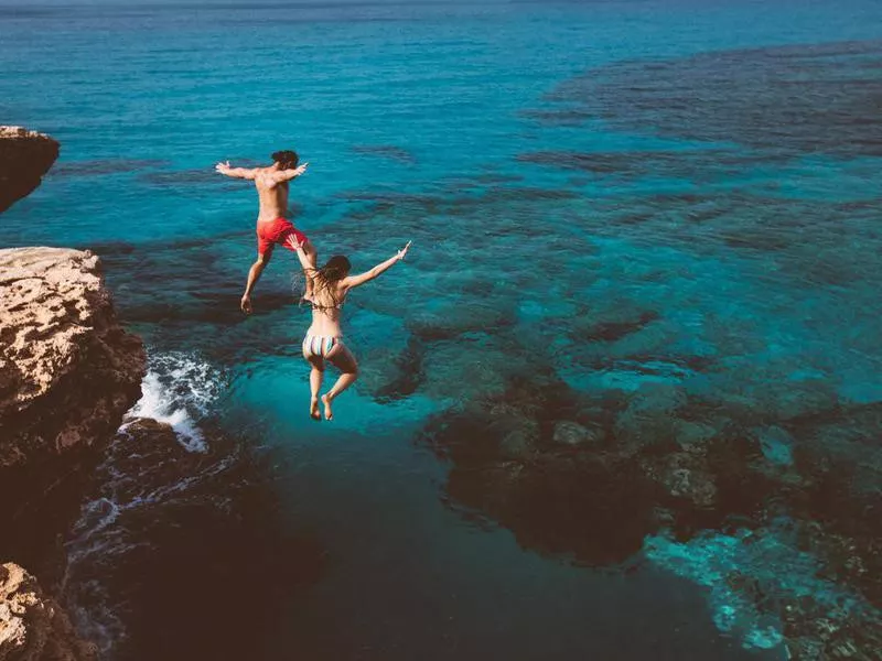 Young brave divers couple jumping off cliff into ocean