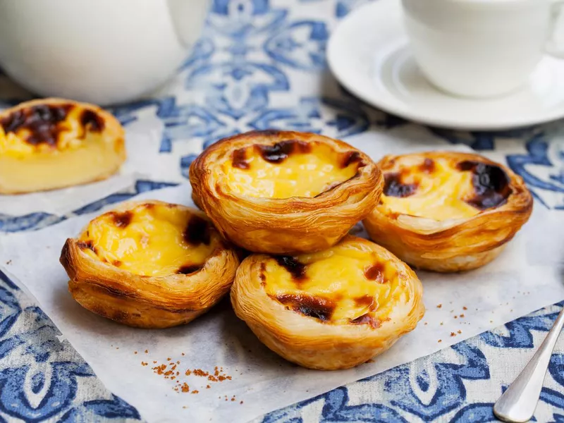 Egg tart, traditional Portuguese dessert, pastel de nata on a parchment paper. Blue background.