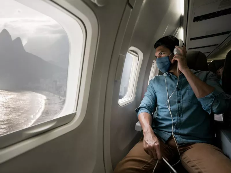 Man traveling by plane wearing a facemask and looking at Rio through the window