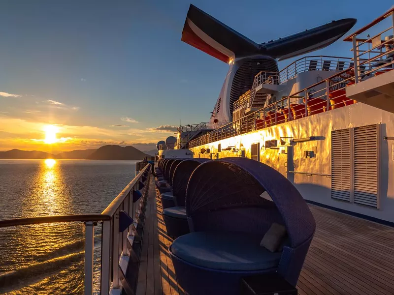 Carnival Legend sailing at sunset in one of the Alaskan Fjords. Sun setting down and mountains in the background. View from the deck in the aft of the ship