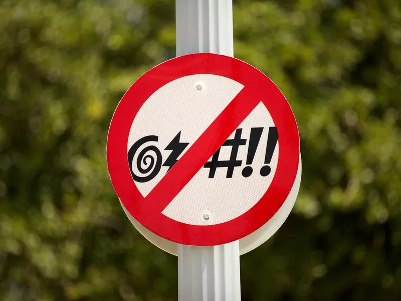 No Cursing Street Sign in front of a green bush