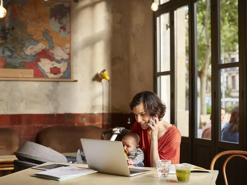 Mother carrying baby using laptop in Barcelona cafe