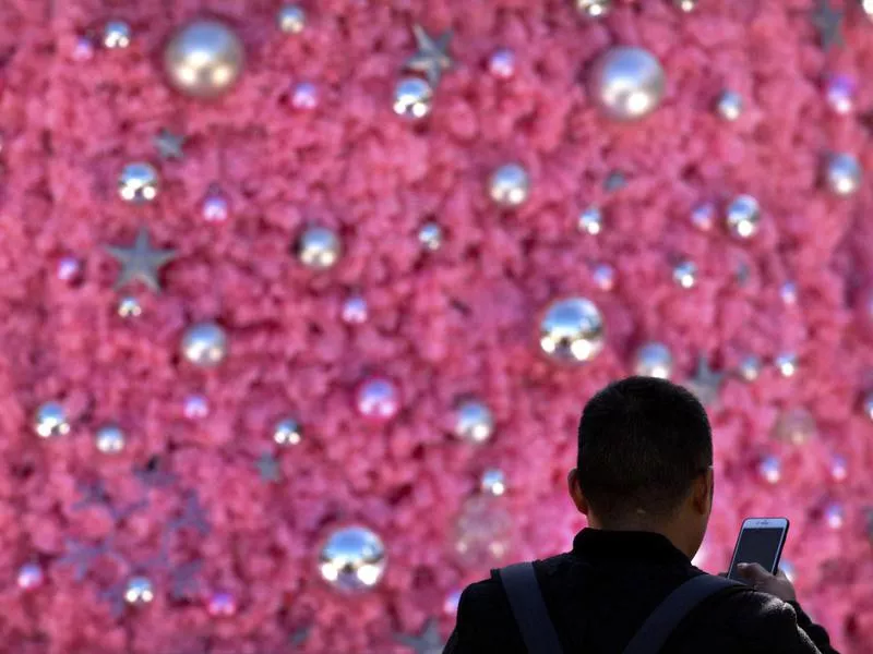 Man holds smartphone as he stands near Christmas display in Beijing