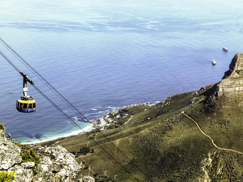 Top down view from Table Mountain of a cable car and the Lion's Head on the right and Atlantic Ocean in the background