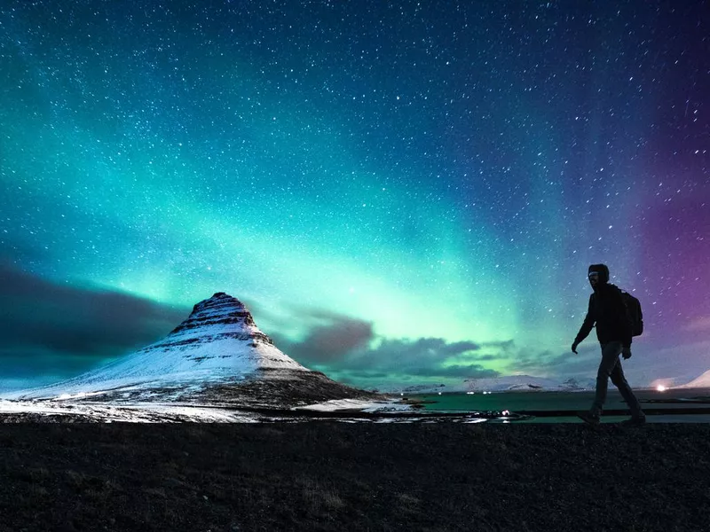 Northern lights in Mount Kirkjufell Iceland with a man passing by