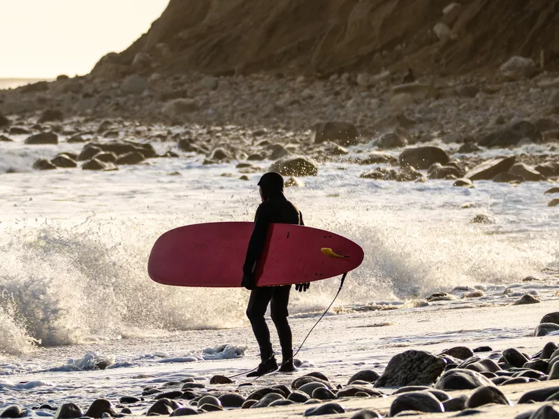 Surfer watching waves crashing on a rocky shore