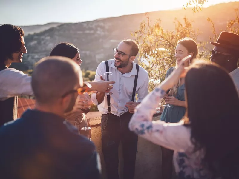 Young elegant multi-ethnic friends drinking wine at countryside cottage party