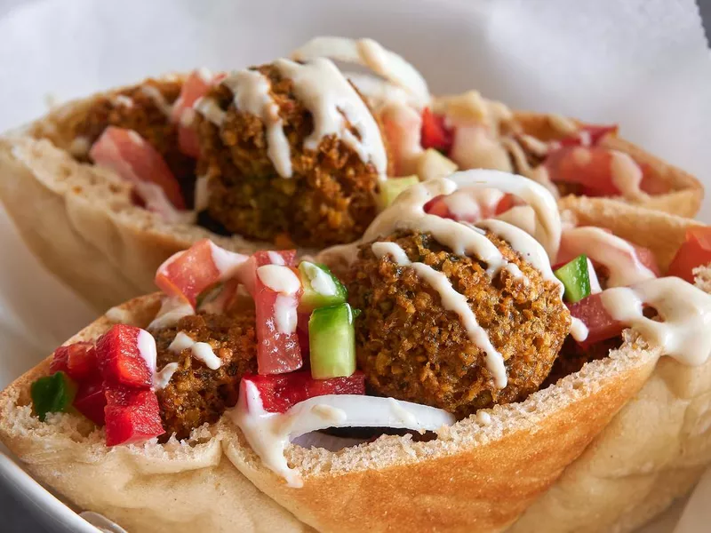 Authentic fresh falafels balls inside of two halves of pita bread sandwich with chopped salad and drizzle of tahini sauce on top, close-up of chickpea falafel in a gluten-free pita