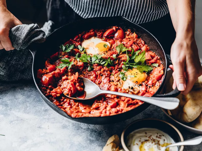 Woman preparing shakshuka with poached eggs