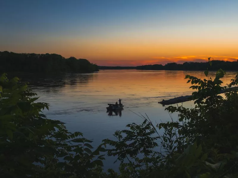 Beautiful view of sunset on big river with fishermen boat ; sunset sky and distant forest in background