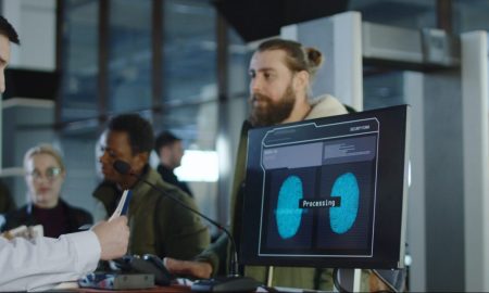 Man giving fingerprints with sensor when passing special control point in airport with employee watching at screen.
